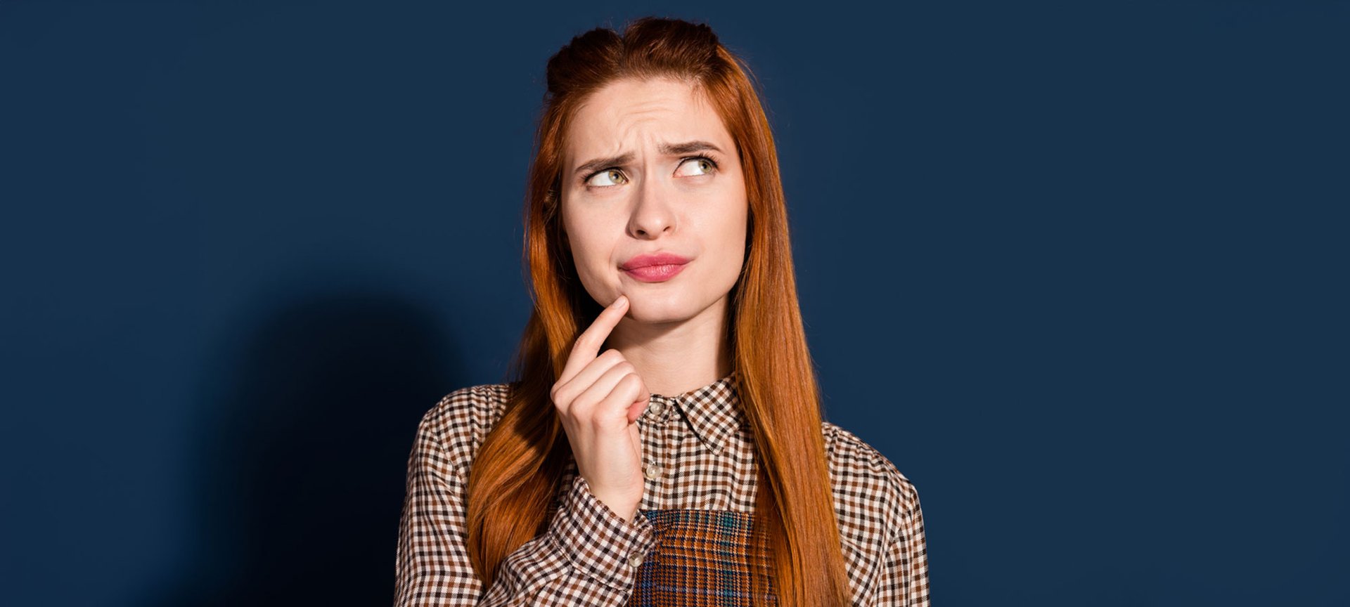 Eine junge Frau mit langen rotbraunen Haaren schaut nachdenklich, vor einer blaugrauen Hintergrund