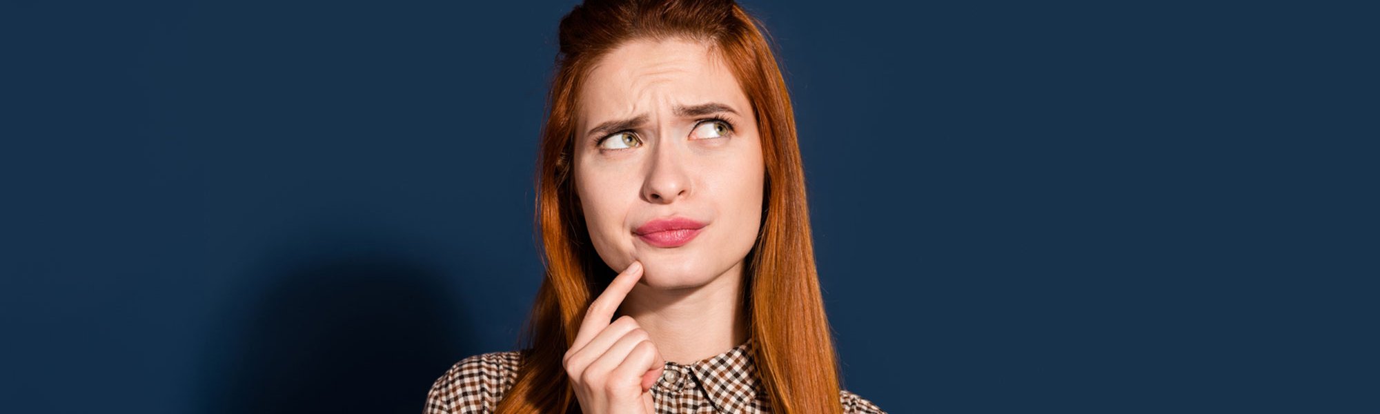 Eine junge Frau mit langen rotbraunen Haaren schaut nachdenklich, vor einer blaugrauen Hintergrund
