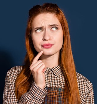 Eine junge Frau mit langen rotbraunen Haaren schaut nachdenklich, vor einer blaugrauen Hintergrund