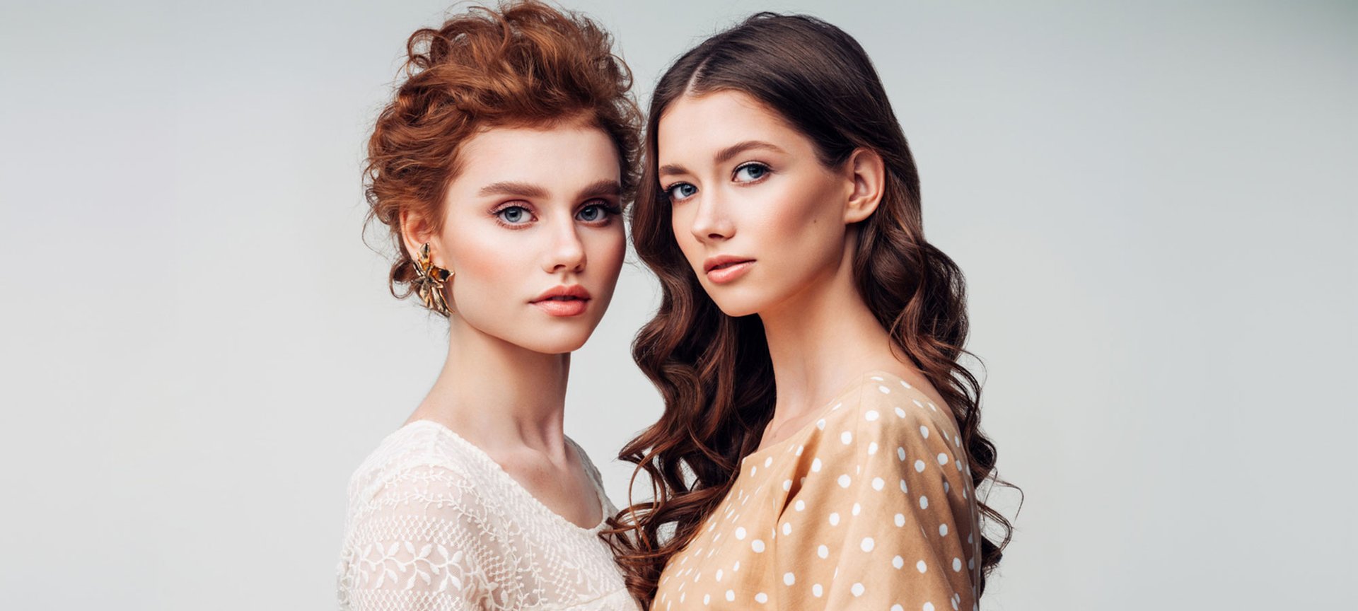 Zwei junge Frauen mit dunkelbraunen und rotbraunen Haaren stehen dicht beieinander und schauen interessiert