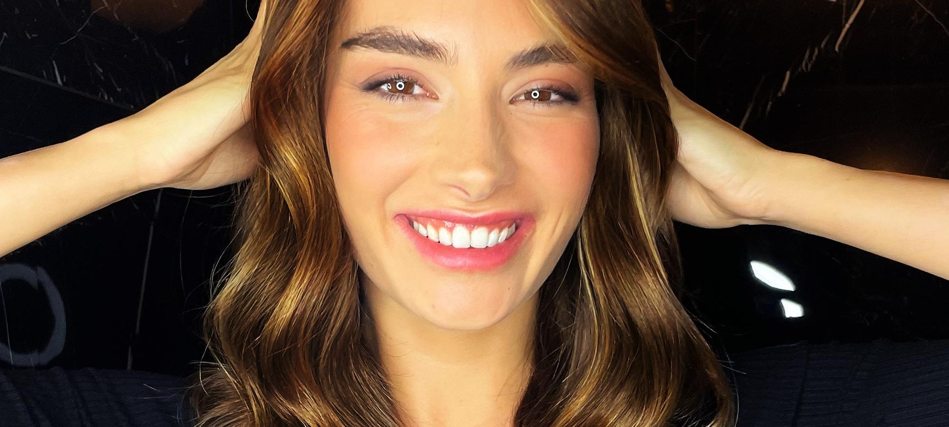 Eine junge Frau greift sich lächelnd in ihre langen Haare