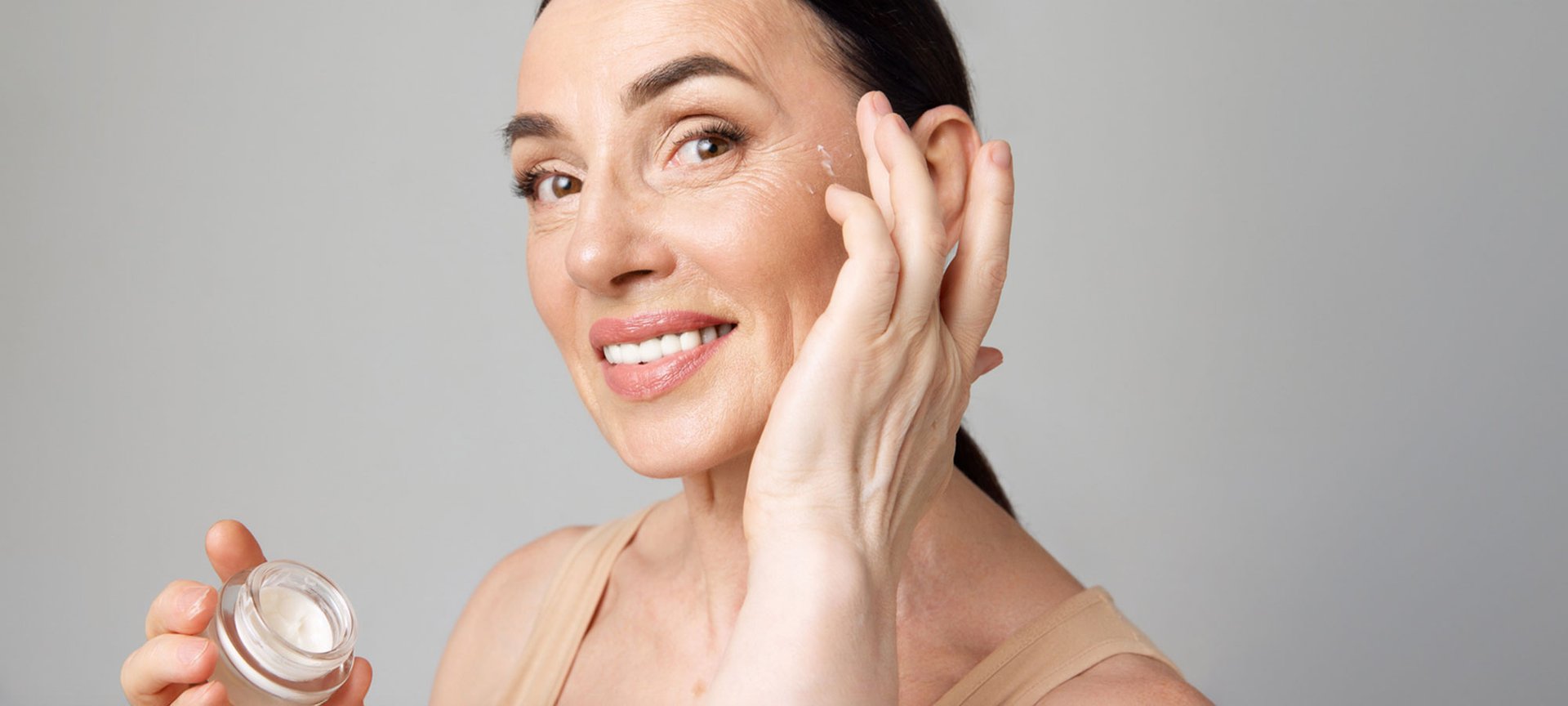 Lächelnde, reife Frau trägt eine Anti-Aging-Creme als Alternative für Botox in das Gesicht auf