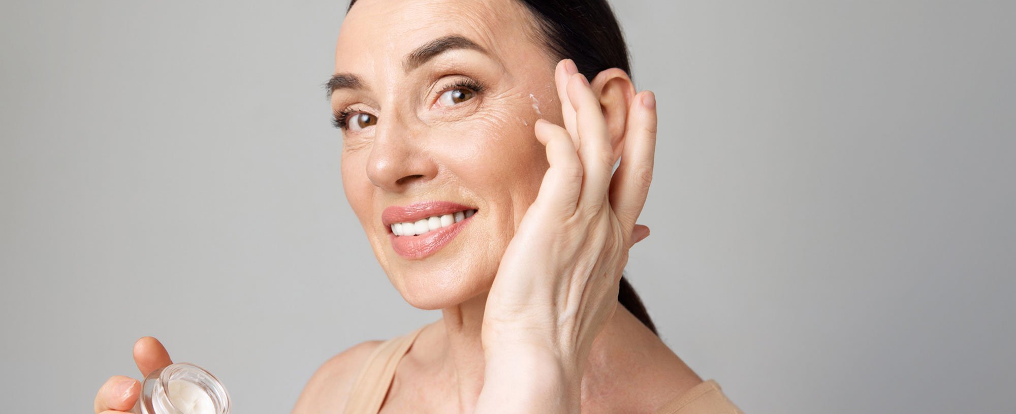 Lächelnde, reife Frau trägt eine Anti-Aging-Creme als Alternative für Botox in das Gesicht auf
