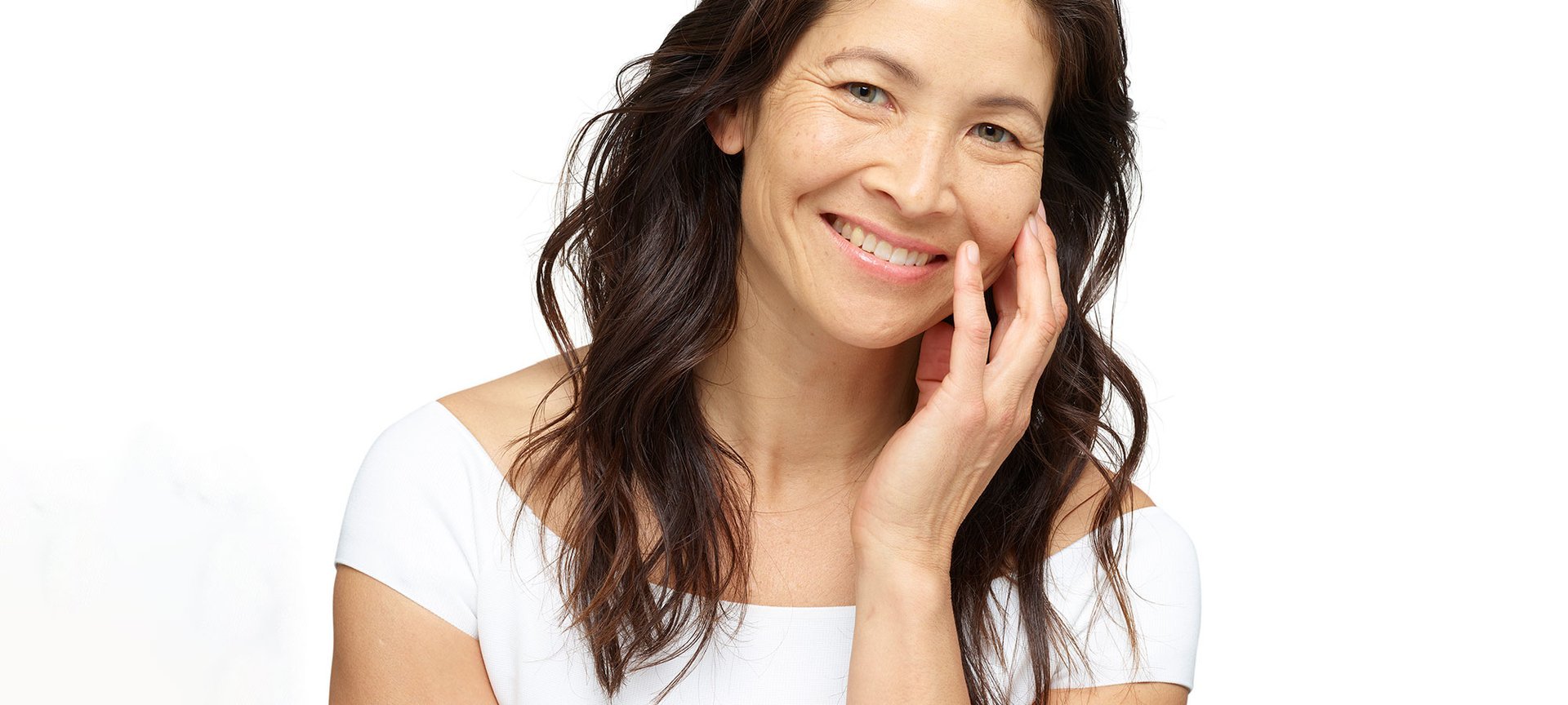 Eine junge Frau, lächelnd mit langen schwarzen Haaren fühlt ihre linke Wange