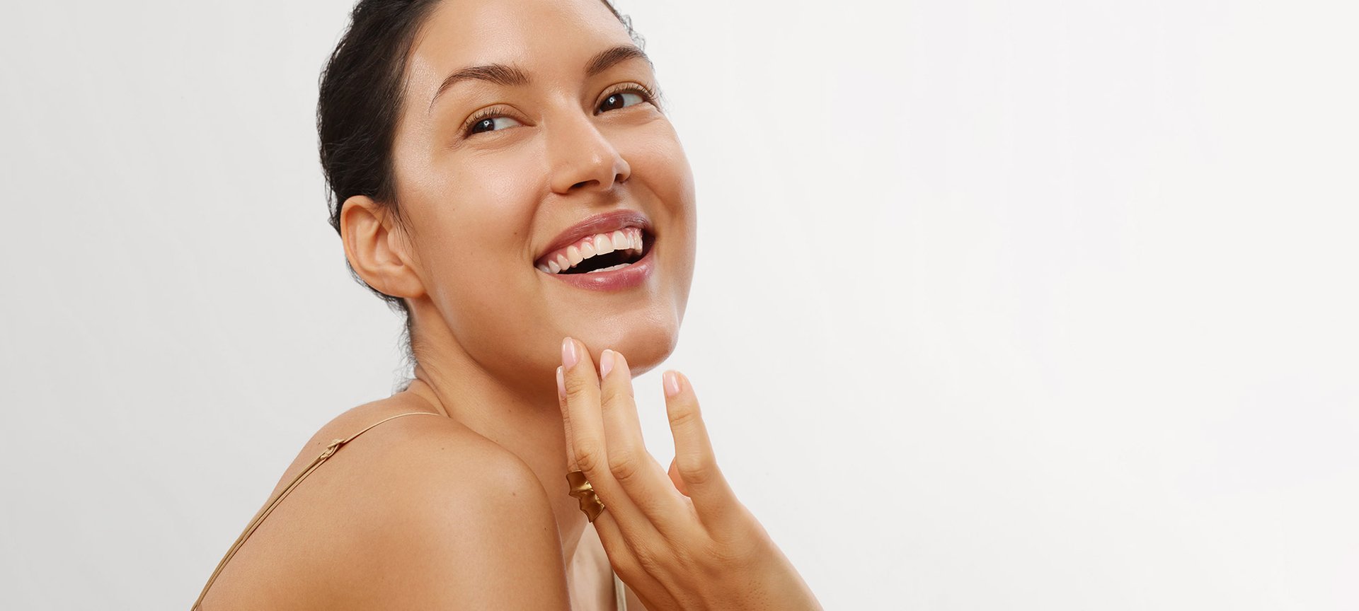 eine lächelnde junge Frau fährt sich mit ihrer Hand über ihren Kinnbereich