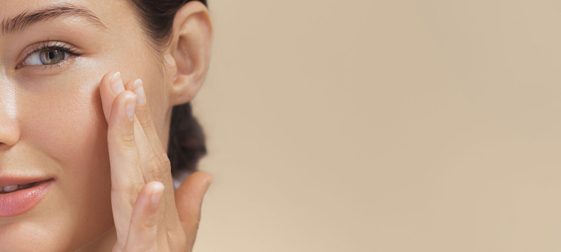 Frontalansicht der linken Gesichtshälfte einer jungen Frau. Sie lächelt leicht und befühlt mit der linken Hand ihre linke Wange.