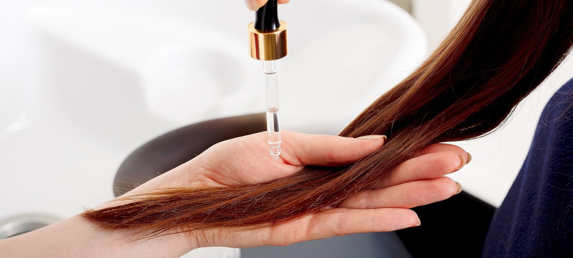 Person haelt eine HAarstraehne in der Hand und traeuffelt Oel darauf