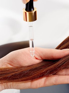 Person haelt eine HAarstraehne in der Hand und traeuffelt Oel darauf