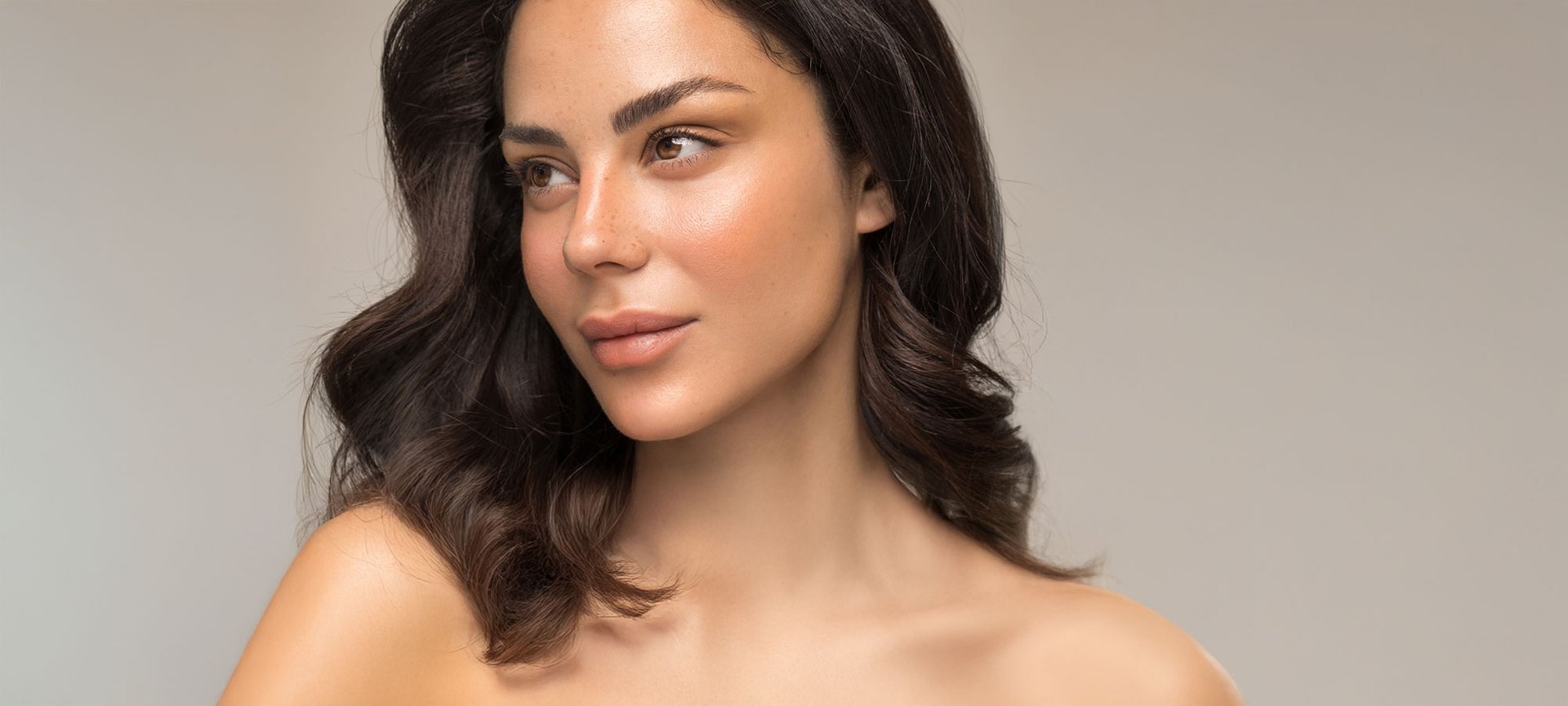 Eine schöne Frau mit glänzender, voller Gesichtshaut und braunen Haaren sieht zur Seite.