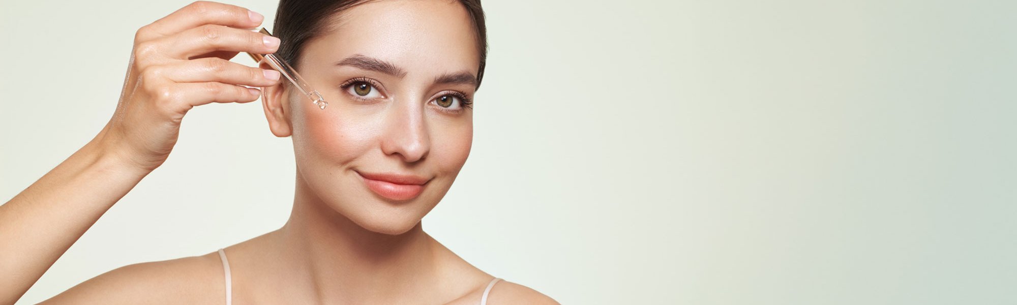 Eine Frau trägt sich mit einer Pipette Retinol auf ihr Gesicht.