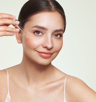 Eine Frau trägt sich mit einer Pipette Retinol auf ihr Gesicht.