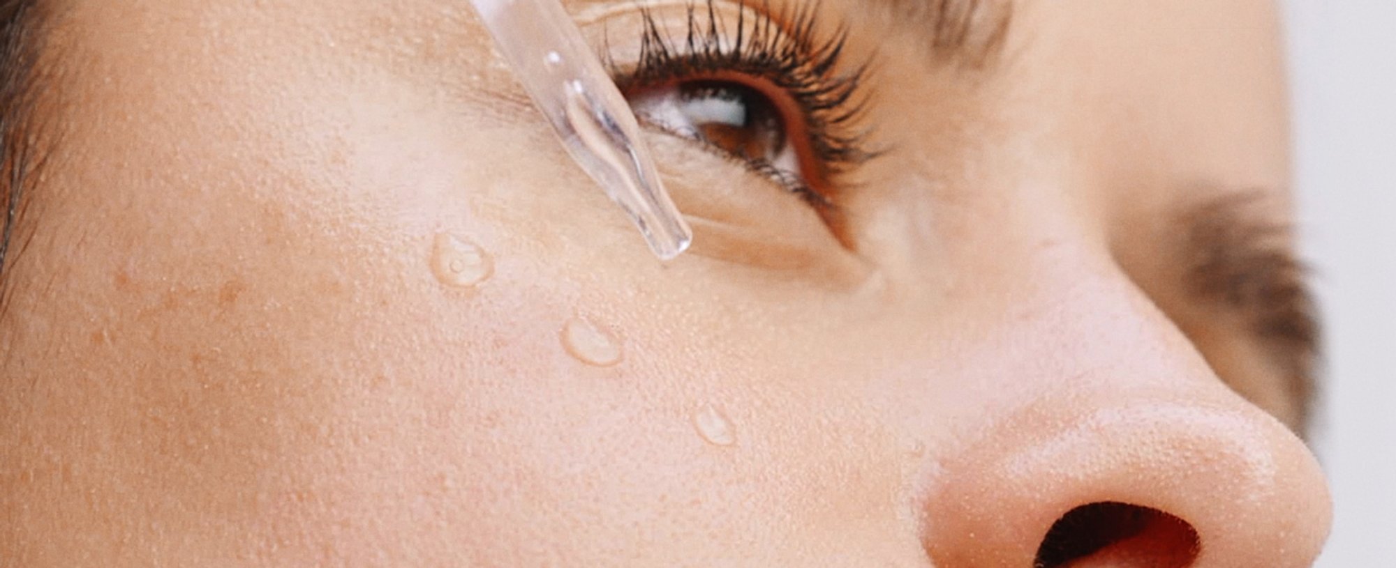Brünette Frau trägt Serum aus einer Pipette auf ihre Wange auf