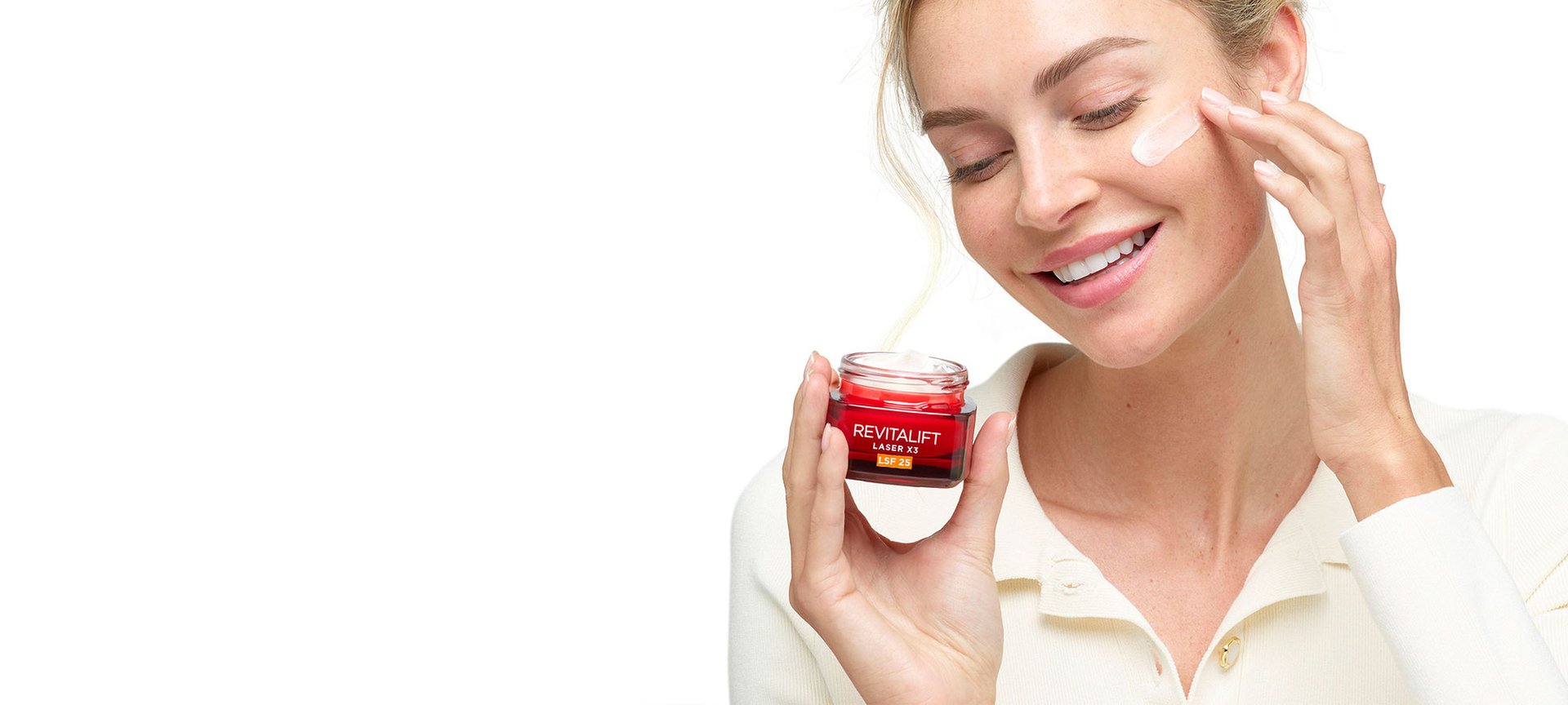 Eine junge Frau verteilt eine Tagescreme auf ihrer linken Wange