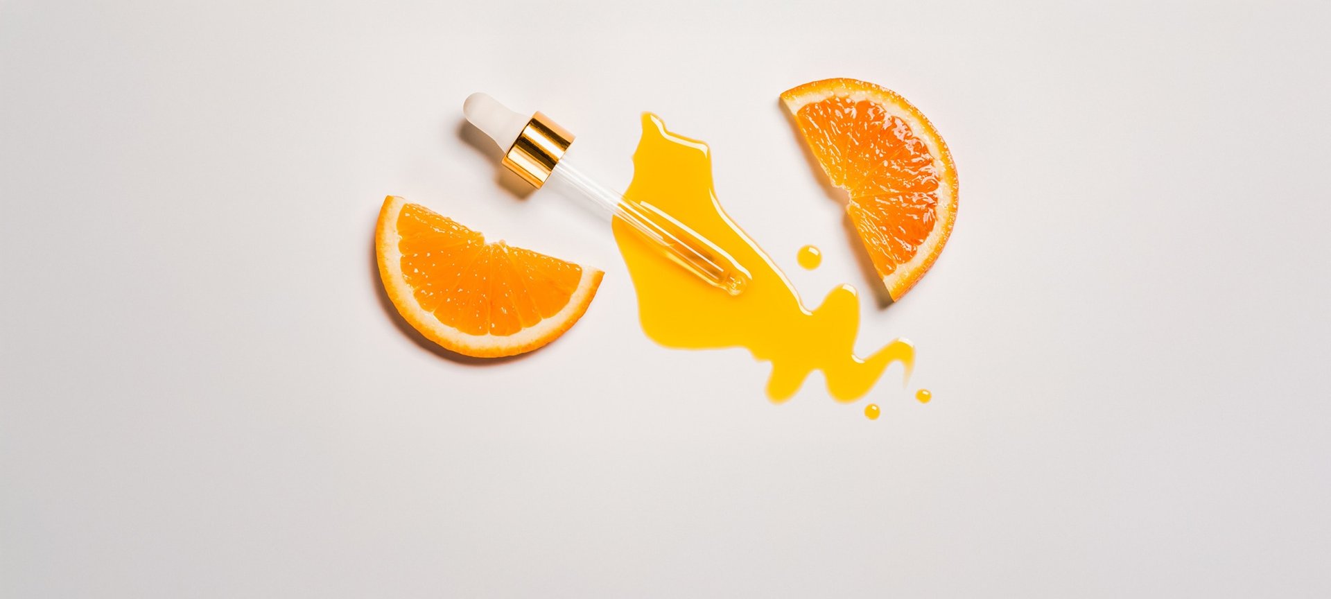 Pipette mit orangener Flüssigkeit und zwei halben Scheiben Orangen auf weißem Hintergrund.