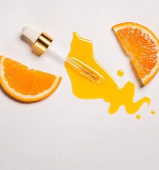 Pipette mit orangener Flüssigkeit und zwei halben Scheiben Orangen auf weißem Hintergrund.
