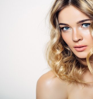 Nahaufnahme einer Fraul mit langen, welligen, bronden Haaren, natürlichem Make-up und blauen Augen.
