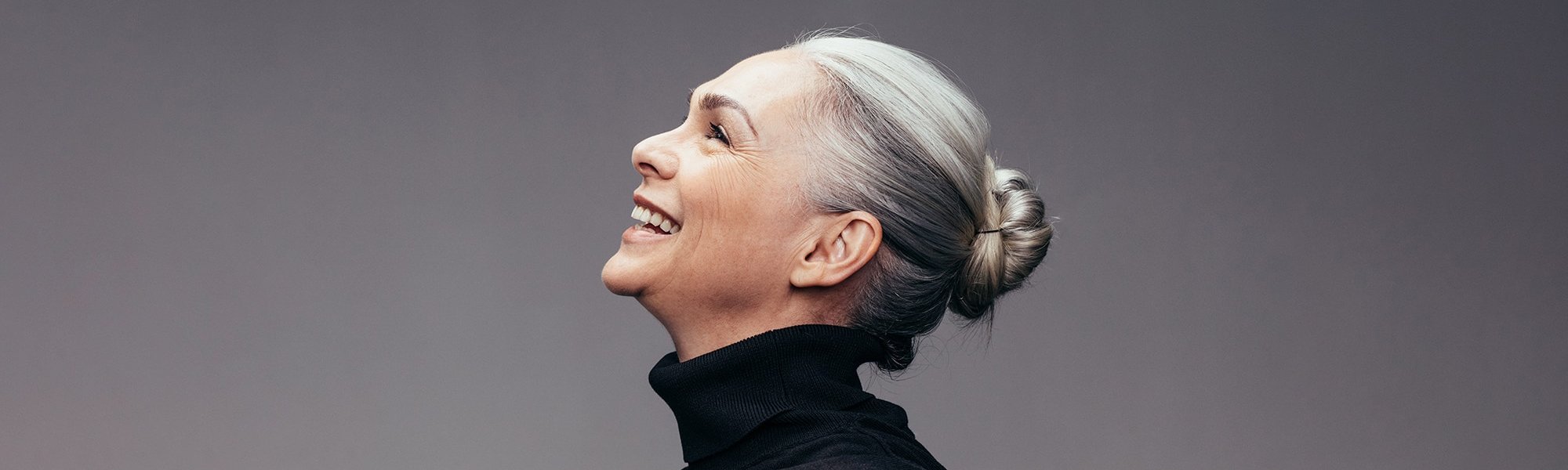 Frau im Profil mit grauen Haaren schaut lächelnd nach oben