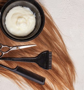 Tönung, Schere, Bürste und Kamm auf braunem Haarschopf