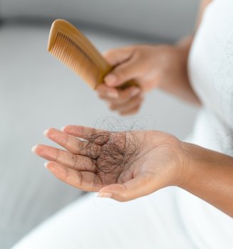Nahaufnahme einer Frau, die einen Büschel schwarzer Haare in einer Hand hält und einen Kamm der anderen