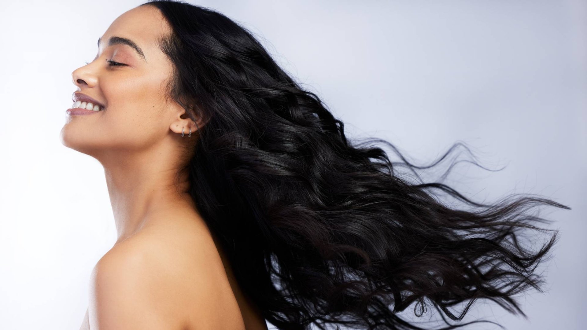Junge, lächelnde Frau mit wehenden, glänzenden, langen schwarzen Haaren, die seitlich zur Kamera steht