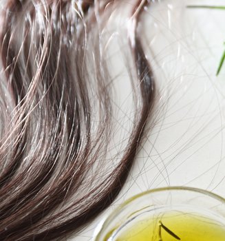 Kleine Flasche, Schale und Pipette mit Rosmarinöl neben Rosmarinzweigen und Haarsträhnen