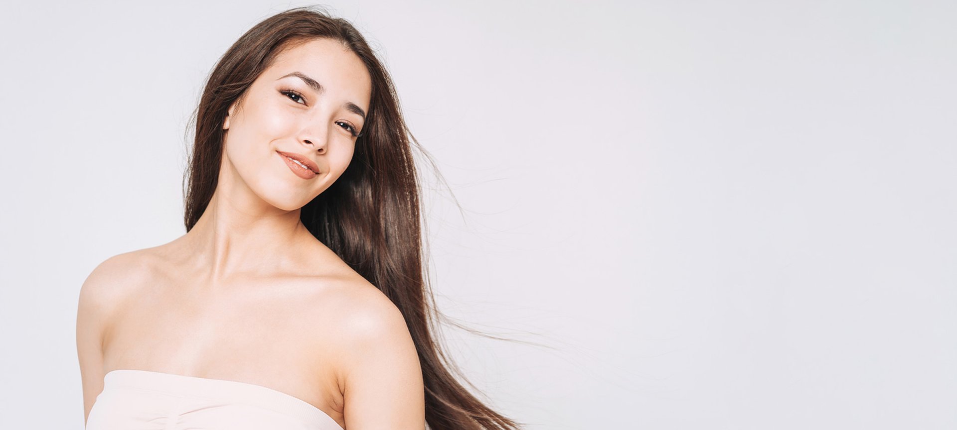 Junge Frau mit braunen feinen Haaren vor grauem Hintergrund.