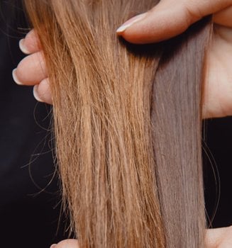 Langes braunes Haar wird von zwei Händen gehalten