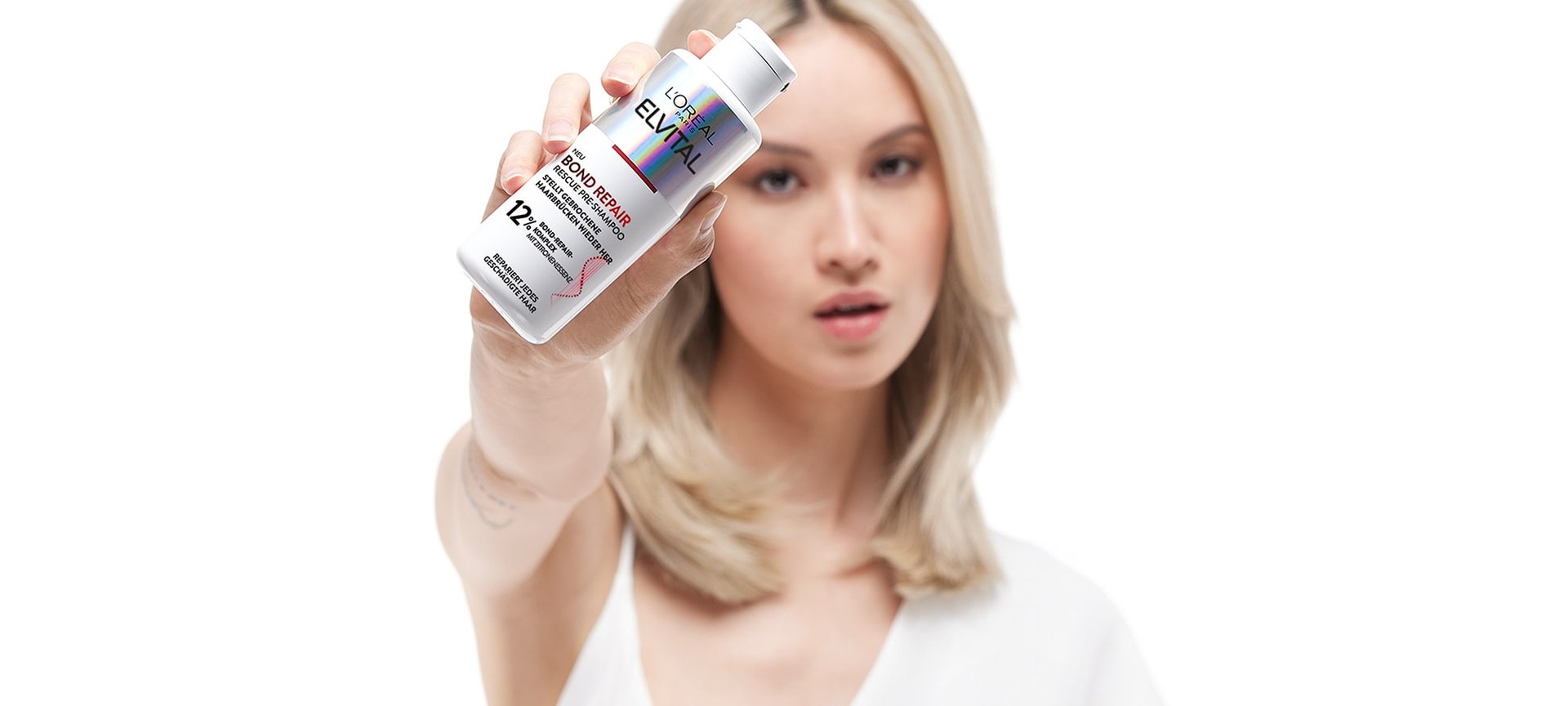 Blonde Frau hält das Elvital Bond Repair Rescue Pre-Shampoo in der Hand