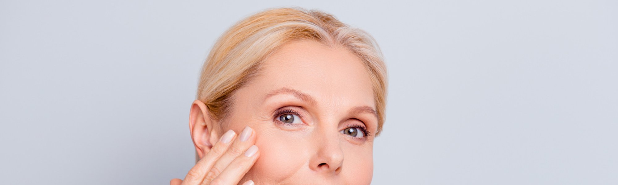 Eine blonde Frau blickt in die Kamera und befühlt mit ihrer rechten Hand ihre rechte Wange.