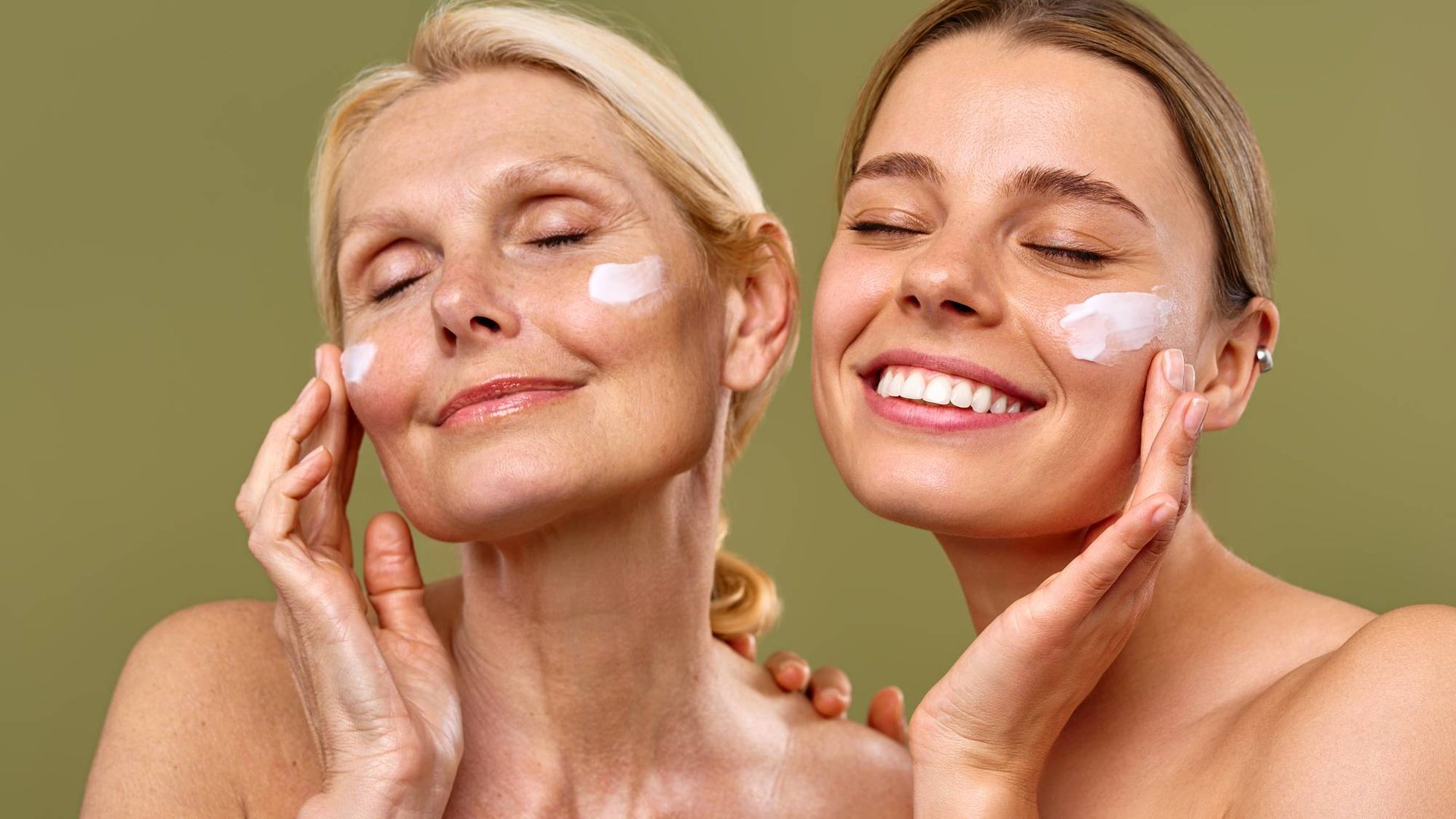 Blonde, lächelnde Mutter und Tochter mit geschlossenen Augen und Anti-Aging-Creme auf den Wangen