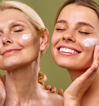 Blonde, lächelnde Mutter und Tochter mit geschlossenen Augen und Anti-Aging-Creme auf den Wangen