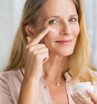 Eine Frau trägt Creme auf die Haut unter ihrem Auge auf.