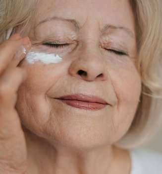 Eine ältere Dame mit geschlossenen Augen trägt Augencreme unter ihrem Auge auf