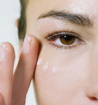 Nahaufnahme vom Gesicht einer jungen Frau mit Augencreme in drei Punkten unter den Augen