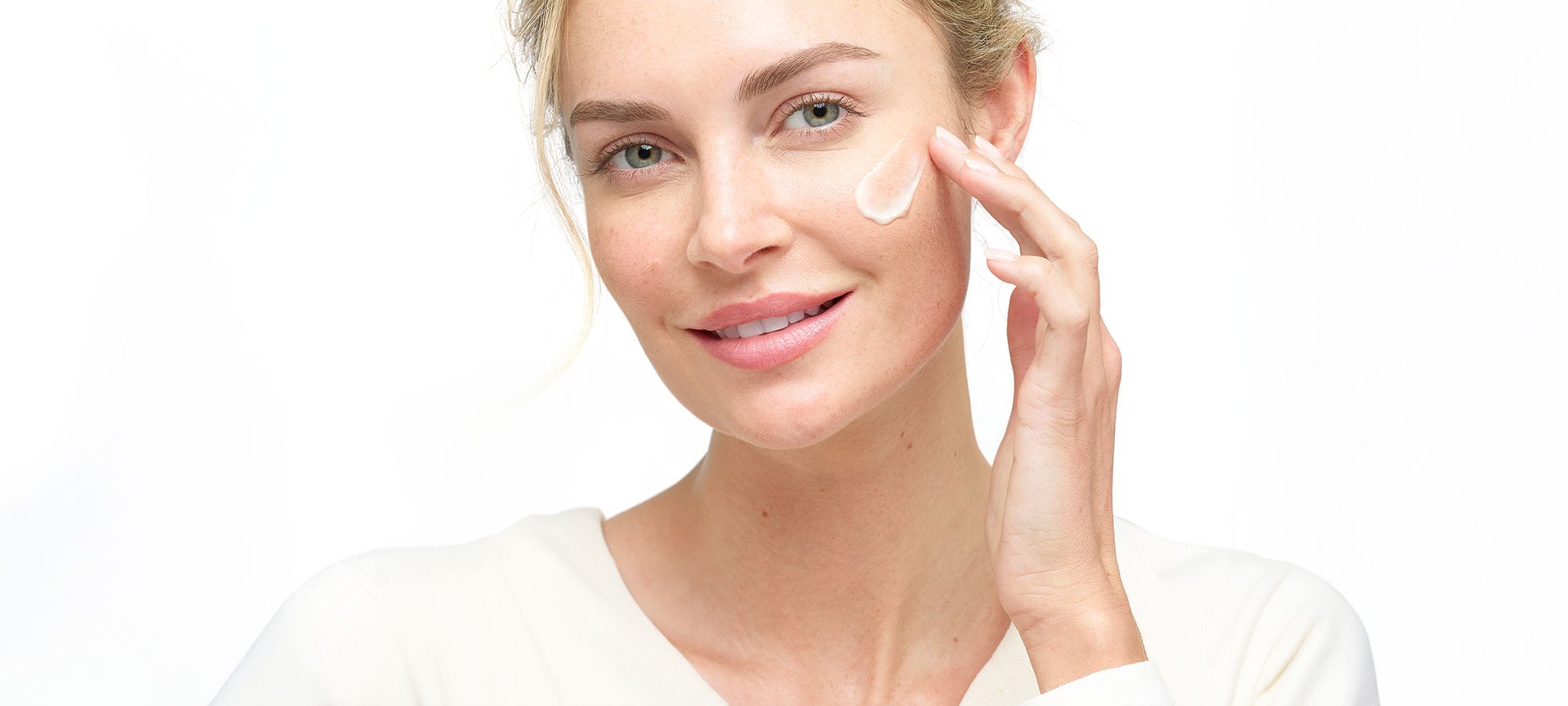 Eine junge Frau verteilt eine Hautcreme auf ihrer linken Wange