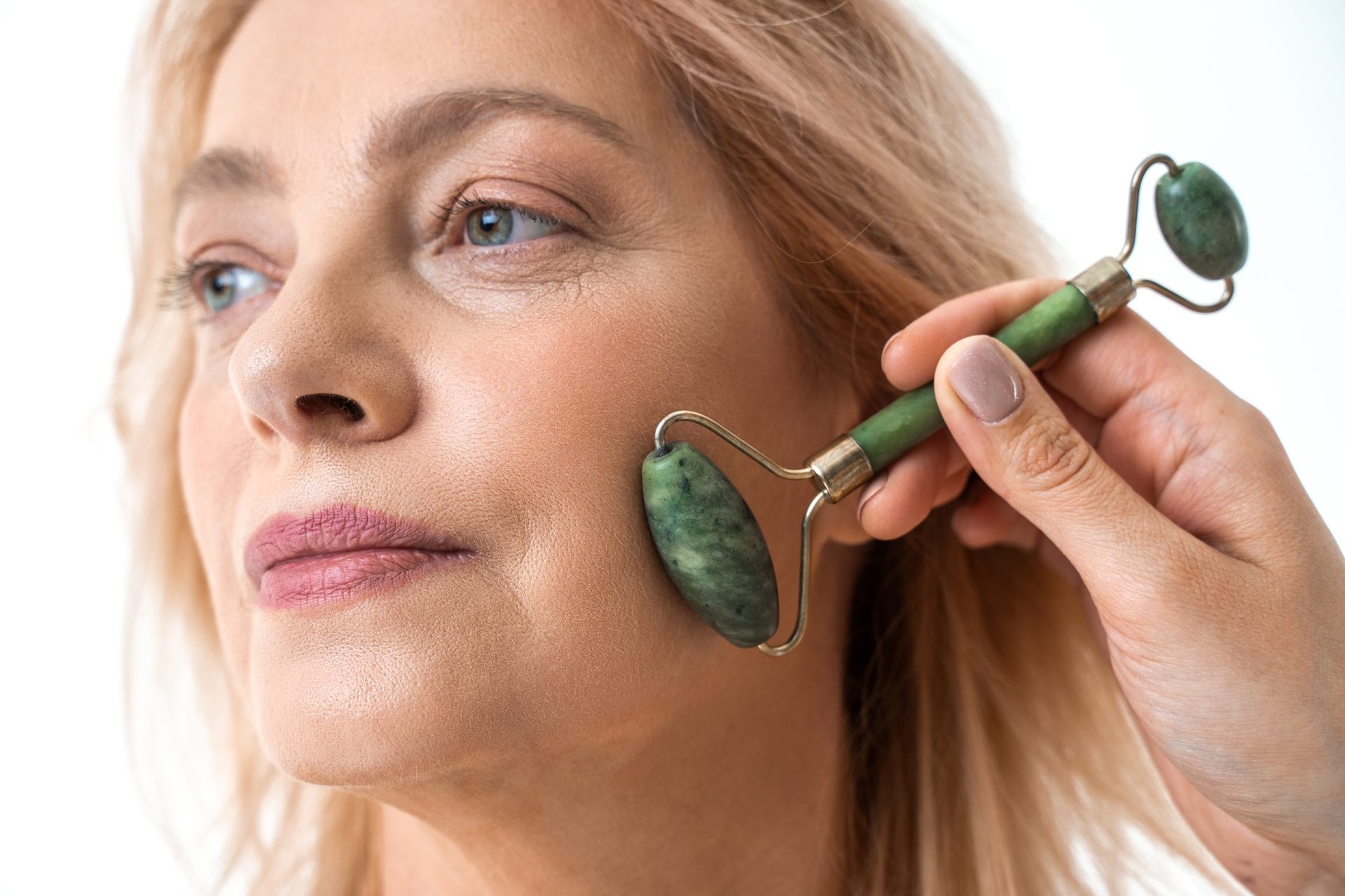 Frau massiert ihr Gesicht mit einem grünen Jade-Roller.