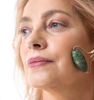 Frau massiert ihr Gesicht mit einem grünen Jade-Roller.