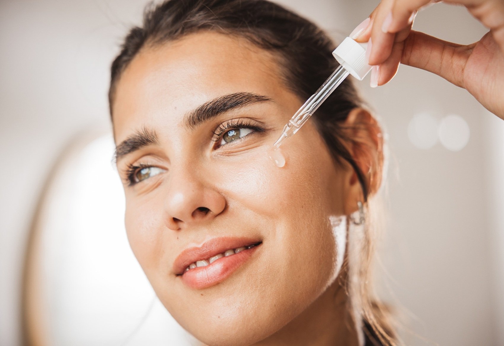 Junge Frau trägt mit einer Pipette ein Hyaluronsäure-Serum auf ihre Wange auf