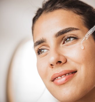 Junge Frau trägt mit einer Pipette ein Hyaluronsäure-Serum auf ihre Wange auf