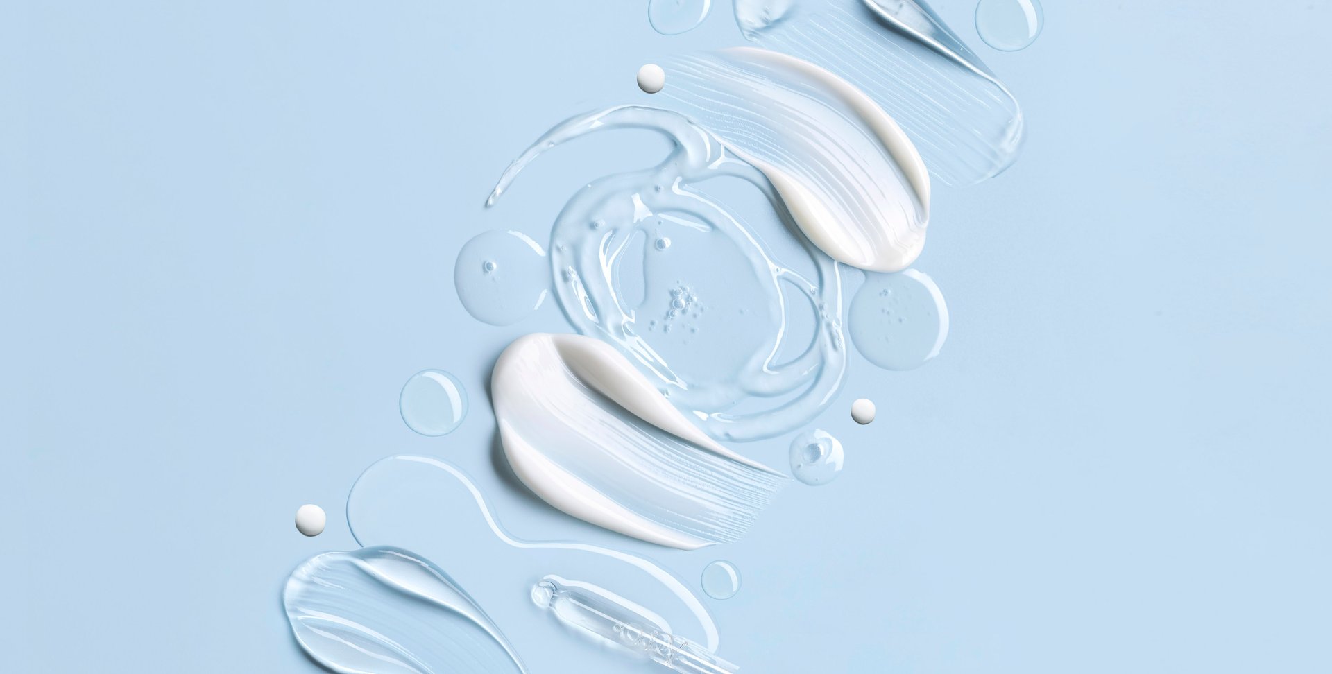 Weiße Creme, transparentes Gel und Tropfen als Texturen auf hellblauem Hintergrund