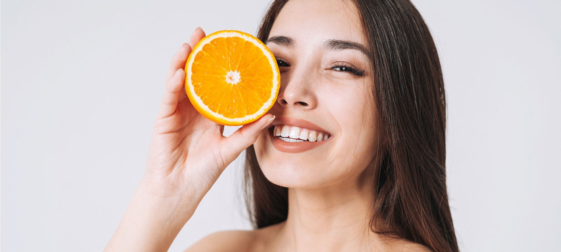 Lächelnde Frau hält sich eine halbe Orange vor ihr Gesicht.