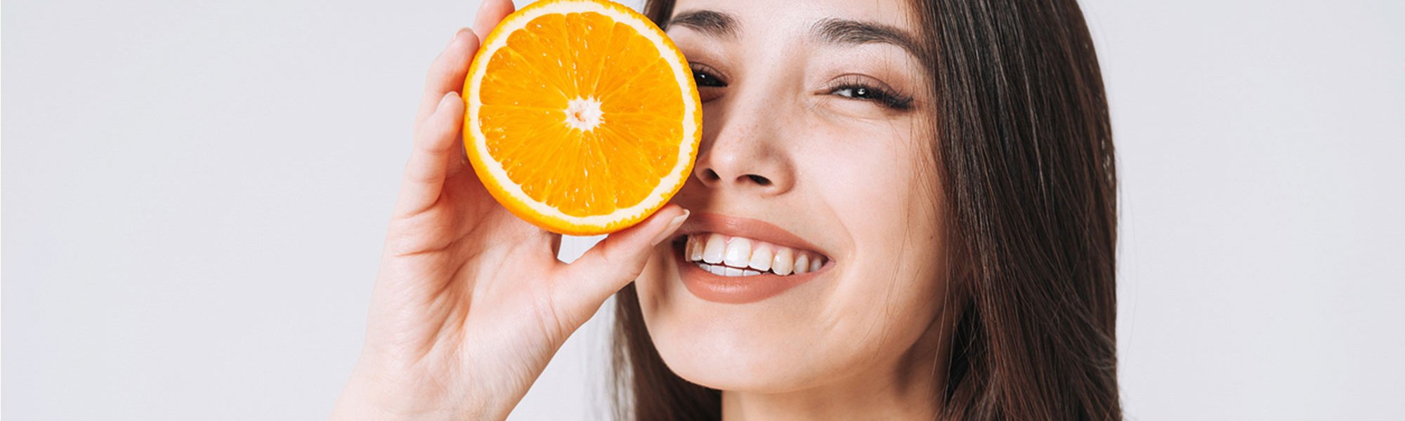 Lächelnde Frau hält sich eine halbe Orange vor ihr Gesicht.