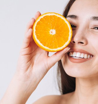 Lächelnde Frau hält sich eine halbe Orange vor ihr Gesicht.