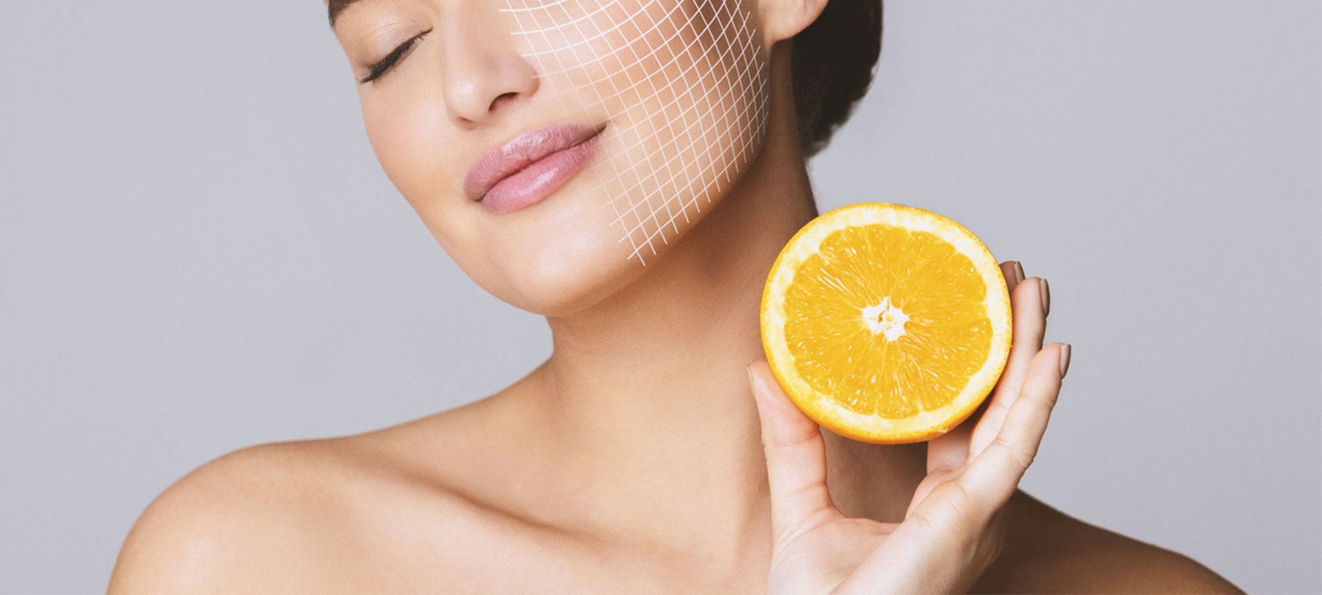Dunkelhaarige Frau mit geschlossenen Augen hält eine Orangenscheibe auf Halshöhe, die eine Gesichtshälfte ist mit digitalen Rasterlinie überzogen.