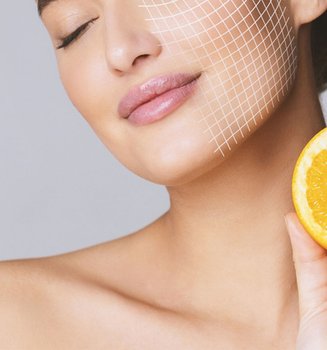 Dunkelhaarige Frau mit geschlossenen Augen hält eine Orangenscheibe auf Halshöhe, die eine Gesichtshälfte ist mit digitalen Rasterlinie überzogen.