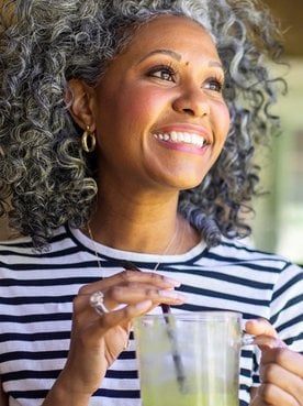 Lächelnde Frau mit lockigem silbergrauen Haaren schaut aus dem Fenster