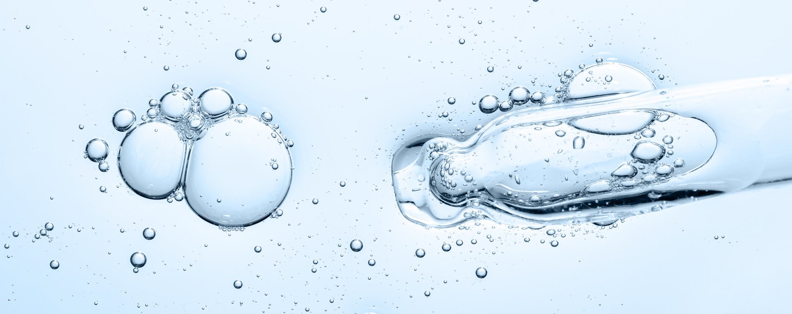 Closeup einer Pipettenspitze in hellblauer Flüssigkeit mit Luftblasen