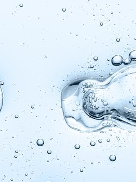 Closeup einer Pipettenspitze in hellblauer Flüssigkeit mit Luftblasen