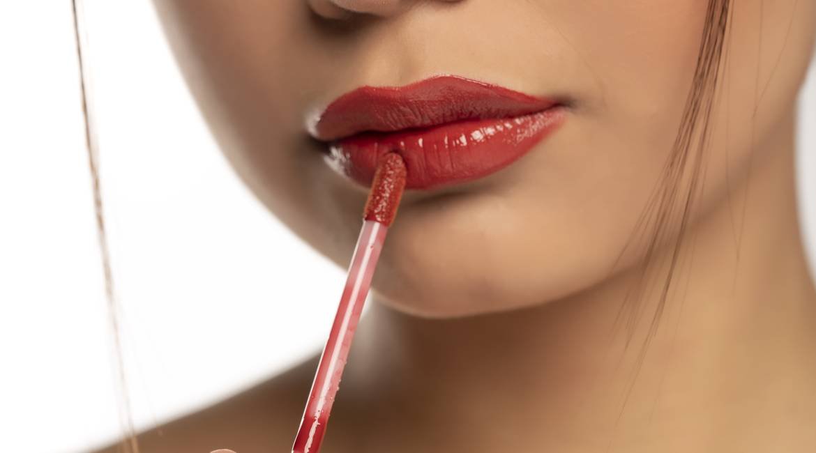 Nahaufnahme der unteren Gesichtshälfte einer jungen Frau, die sich roten Lip Tint  aufträgt