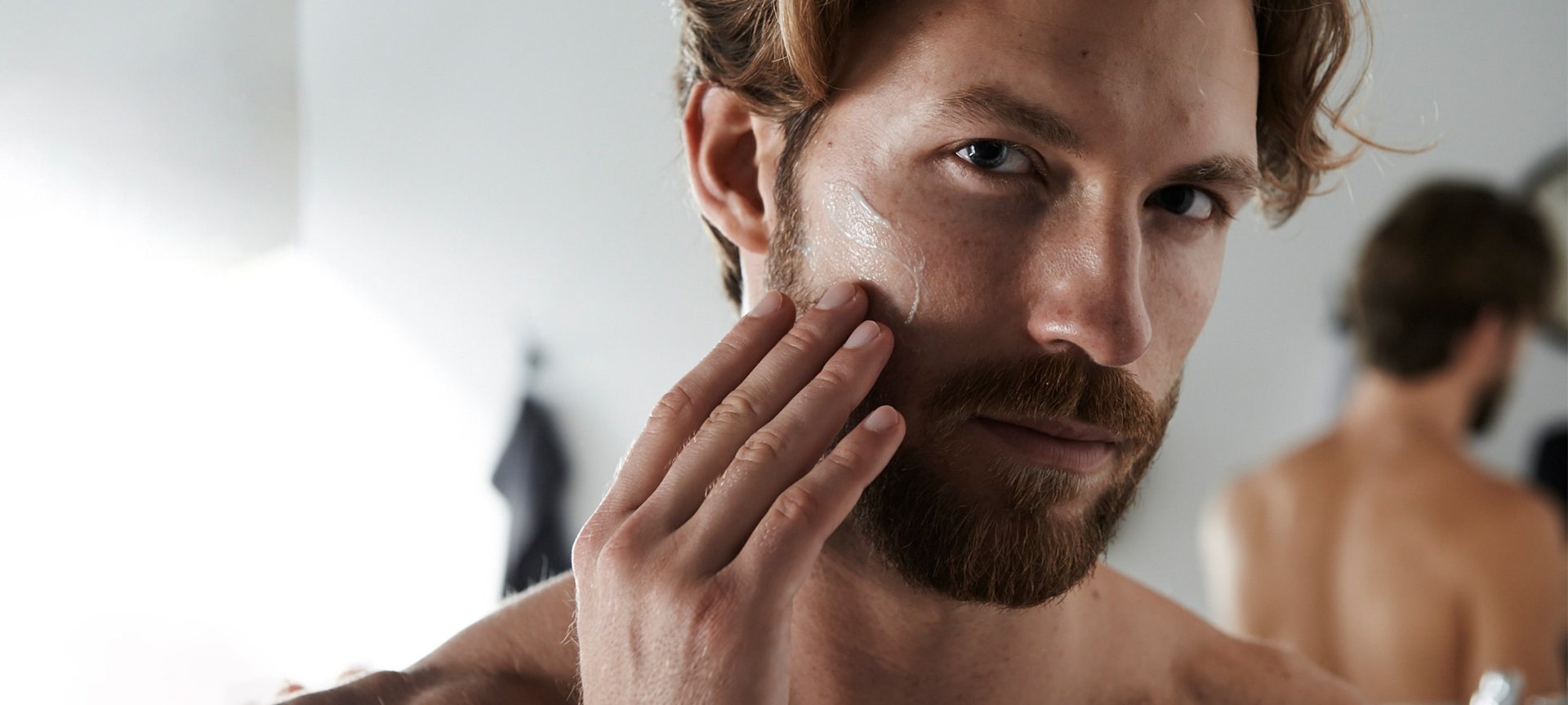 Ein junger Mann betrachtet sich im Spiegel und streicht sich dabei über seinen Bart